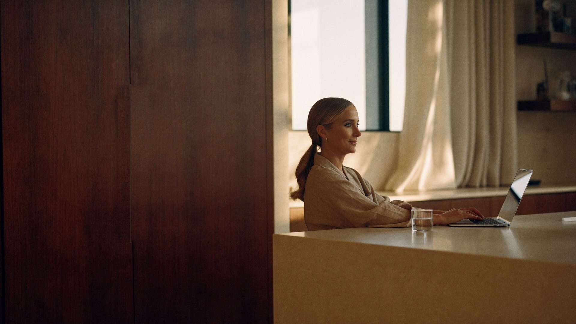 A business owner writing a message on her laptop at her kitchen counter in the early evening