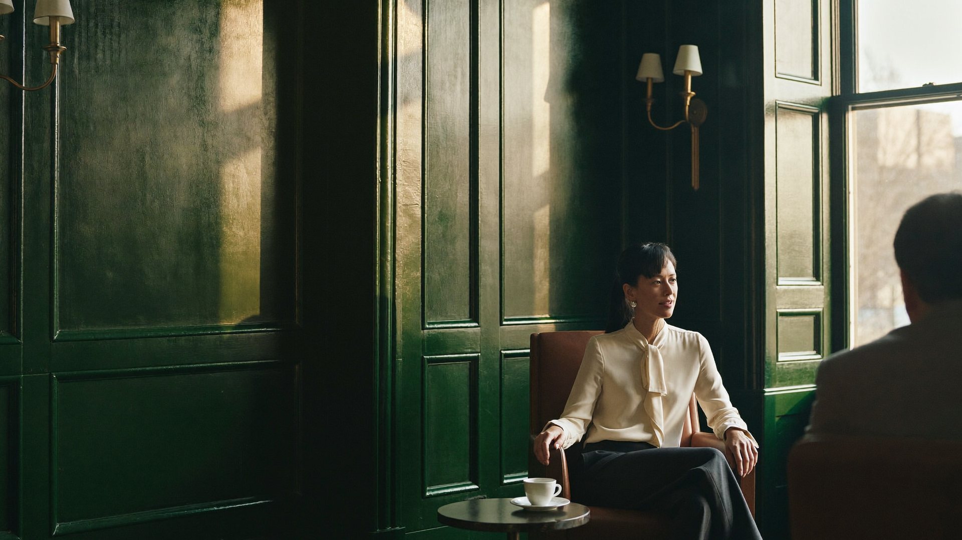 A business owner seated in a green-panelled private study in late light
