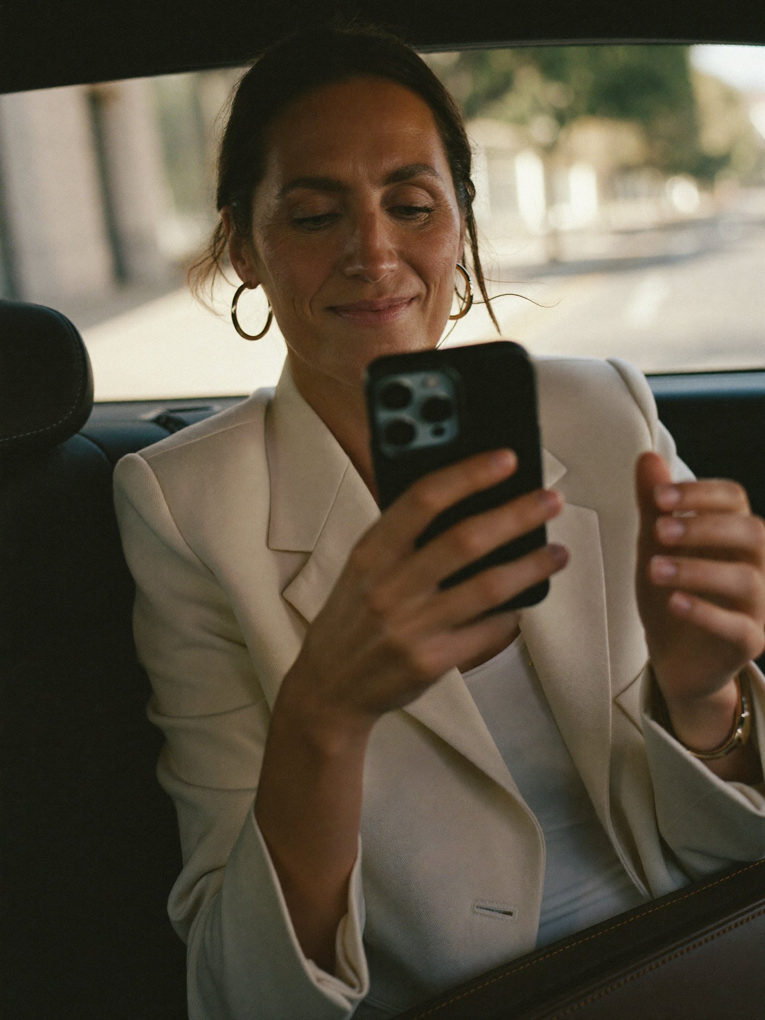 A business owner smiling at a message on her phone in the back of a car