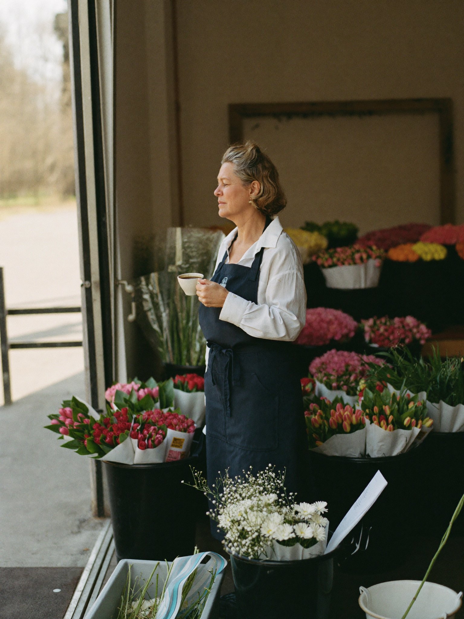 The owner of a flower wholesale business with a coffee among the buckets in her warehouse