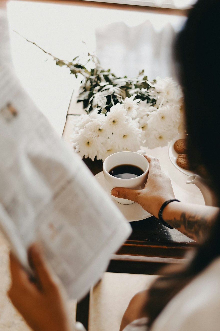 A person reading a newspaper with a cup of coffee in warm morning light