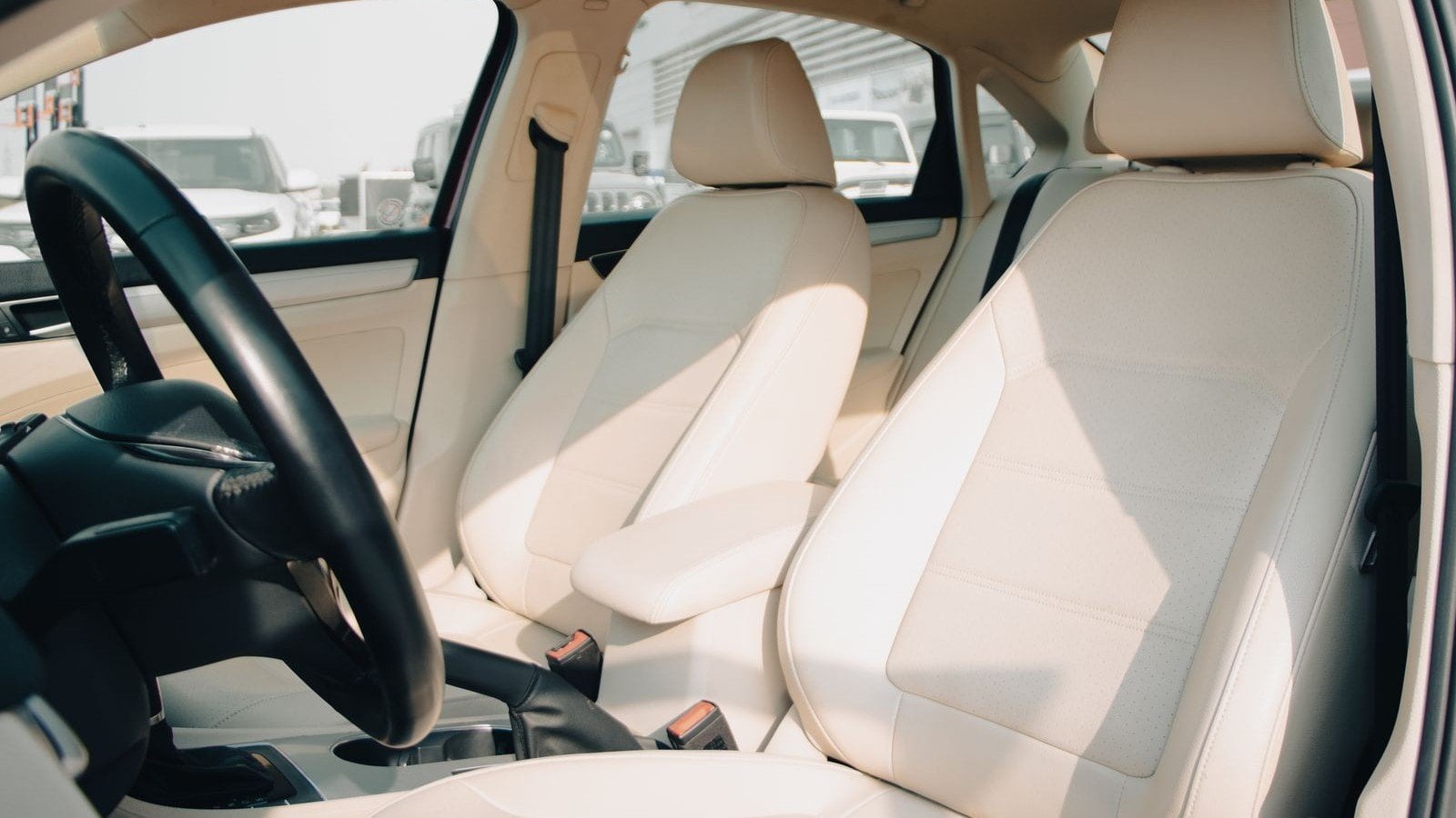 The cream leather front seats of a new car, seen through the open driver's door